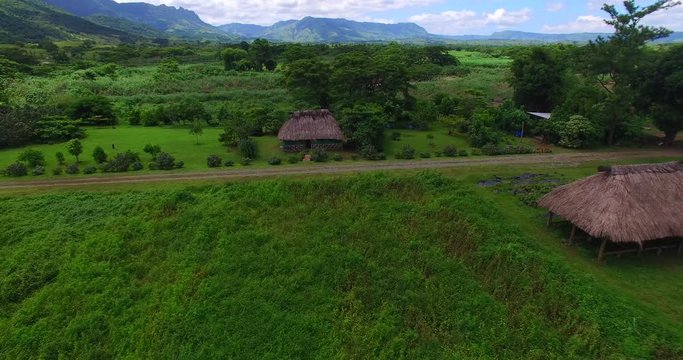 Traditional Fijian Bure in valley with mountainous backdrop and river
