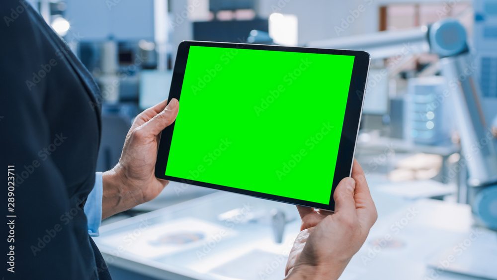 Aufkleber Engineer Holds Green Mock-up Screen Digital Tablet Computer. In the Background Team of Industrial Engineers Working with Functional Robot Arm in Modern Bright Research Facility