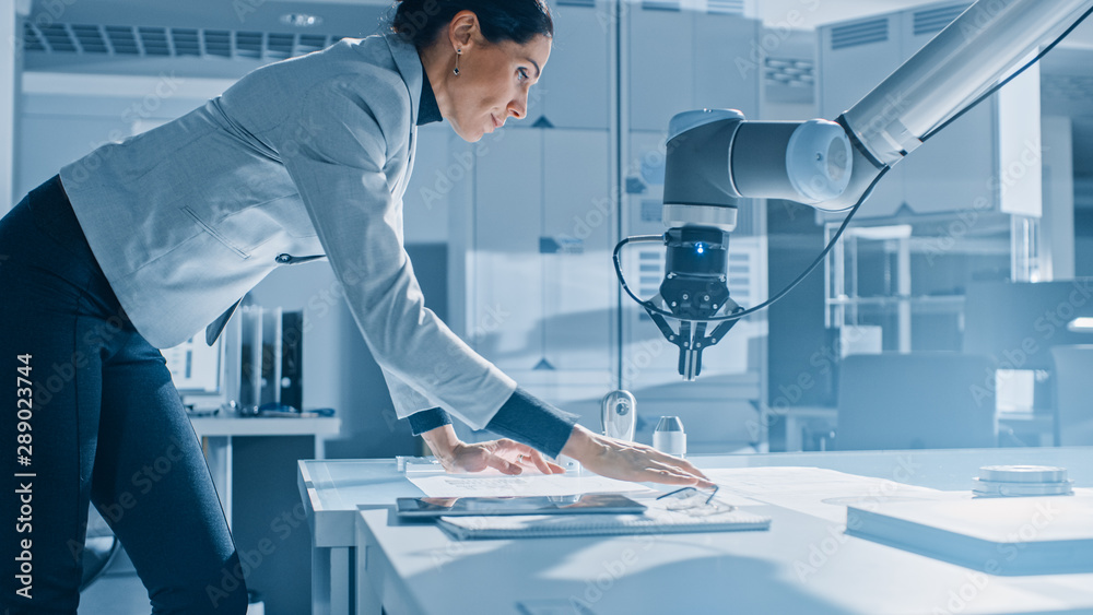 Leinwandbilder stylish female robotics engineer leans on the table works with blueprints, documents and tablet comp