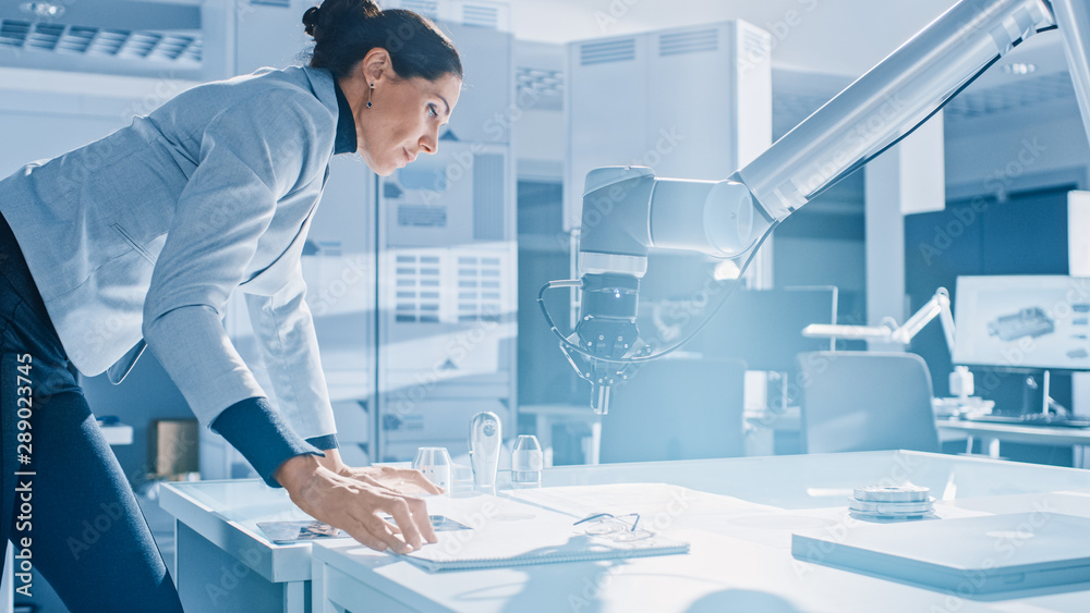 Aufkleber Stylish Female Robotics Engineer Leans on the Table Works with Blueprints, Documents and Tablet Computer, She's Programming Robot Arm Movements