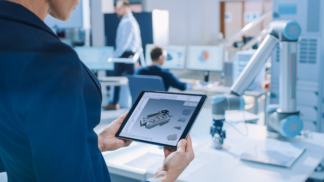 Stylish Female Industrial Robotics Engineer Uses Tablet Computer with CAD Software and to Manipulate and Program Robot Arm for Lifting, Moving Objects. Technology Research Facility for Cloud Computing