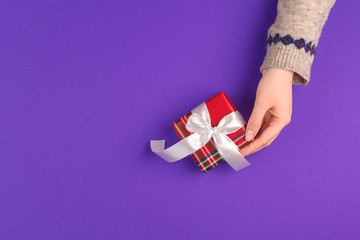 Fototapeta na wymiar Female hands holding wrapped gift on purple background