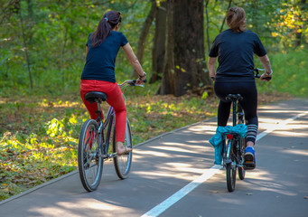 Two women riding bicycles on a Bicycle path in the Park.