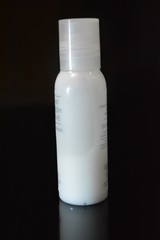 A white small plastic bottle with cosmetic and medical products for body and beauty care is on a glossy black surface.
