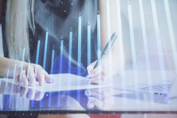 A woman hands writing information about stock market in notepad. Forex chart holograms in front. Concept of research.