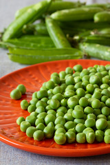 Garden peas on an orange plate with pods on the side.  Grey marl cloth background