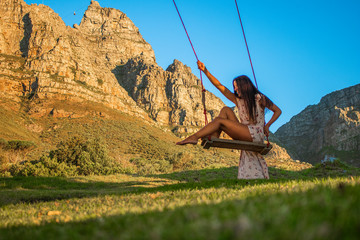 Beautiful woman swinging on a swing in nature with Table Mountain in the background.