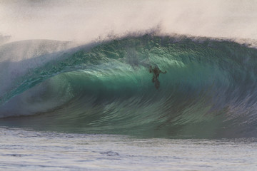 Huge green wave breaking on a shallow reef with a swimmer inside the wave
