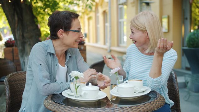 Slow motion of mature ladies in casual clothing socializing in outdoor cafe talking laughing enjoying warm summer day. Friendship and happiness concept.