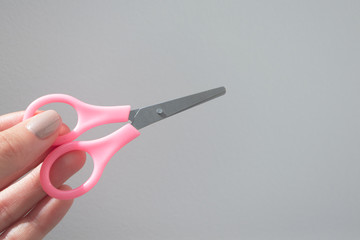 Woman holding сomfortable small stainless steel travel portable scissors on gray background