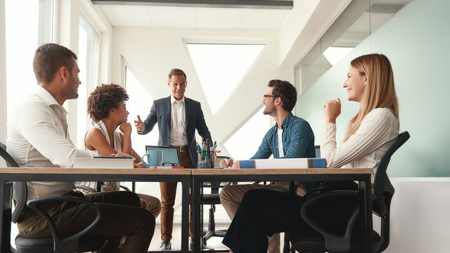 Successful team. Handsome and cheerful mature business man in formal wear discussing something with his colleagues and smiling while working together in the office