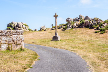 Granite calvary of the chapel of Saint-Nicolas in Bugueles, Brittany, France, on the side of a small country road in front of a granite outcrop on a sunny summer day.