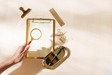 Woman holding magnifying glass over gold stationery on light background
