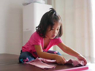 Little Asian baby girl learning to fold her own pants - children help doing household chores
