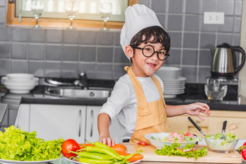 Asian Boy son cooking salad food holdind wooden spoon with vegetable holding tomatoes and carrots, bell peppers on plate for happy family cook food enjoyment lifestyle kitchen in home