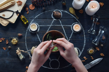 Womens hands make love potion on pentagram circle with candles, stones and old books on witch...