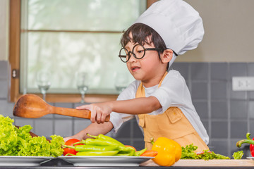 Asian Boy son cooking salad food holdind wooden spoon with vegetable holding tomatoes and carrots, bell peppers on plate for happy family cook food enjoyment lifestyle kitchen in home