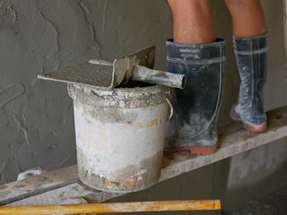 Old dirty grungy bucket and PVC Plastic Trowel on a wooden stand, being used for cement plastering by a construction worker
