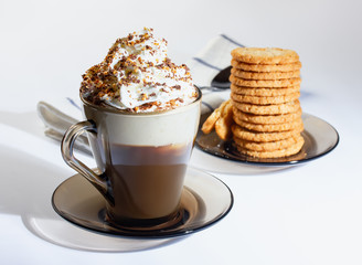 Coffee, cappuccino with whipped cream sprinkled with chocolate chips, ground nuts, cinnamon. Oatmeal cookies, stacked on a plate. Napkin, dessert spoon. The photo.