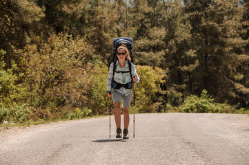 Girl walking on the road with hiking backpack and hiking sticks