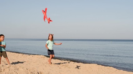 Little boy and girl play on baltic sea sand beach launching red toy plane having fun