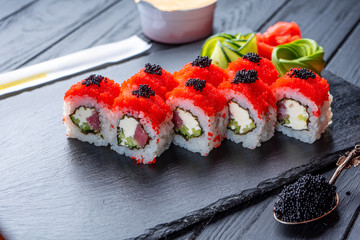 Set of sushi rolls with cream cheese, rice and salmon on a black board decorated with ginger and wassabi on a dark wooden background. Japanese cuisine. Food photo background