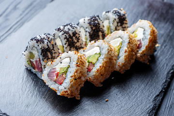 Set of sushi rolls with cream cheese, rice and salmon on a black board decorated with ginger and wassabi on a dark wooden background. Japanese cuisine. Food photo background