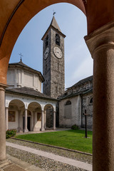The beautiful baptistery and the bell tower of Baveno, Italy, framed by the columns of the portico of the via crucis, in the monumental complex