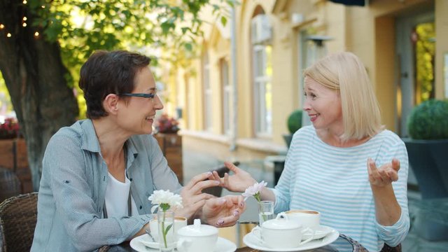 Female friends brunette abd blonde are having good time in street cafe talking laughing sitting at table together. Lifestyle, communication and friendship concept.