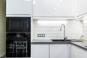 interior of the modern kitchen is white with black furniture and household appliances