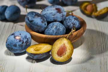 Raw plums in a plate on a white wooden background