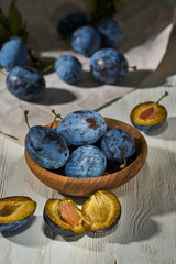 Raw plums in a plate on a white wooden background
