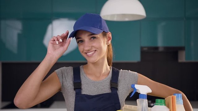Attractive clining service woman with nice smile holding basket with different products and items for cleaning,being in the beautiful kitchen