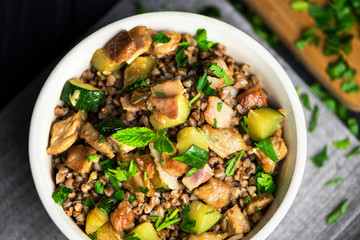 stewed buckwheat porridge with bacon and meat, greens in a bowl on a dark background
