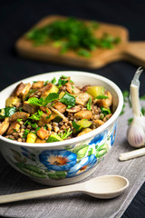 stewed buckwheat porridge with bacon and meat, greens in a bowl on a dark background