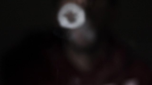 Man in dark background vape blows smoke rings towards screen, close up slow motion