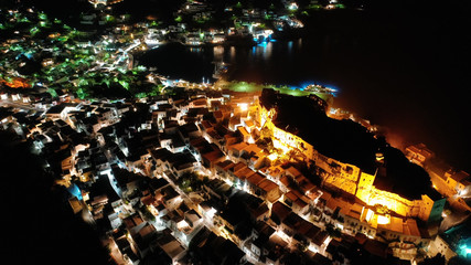 Aerial drone night shot of iconic illuminated medieval fortified castle overlooking the deep blue Aegean sea in Chora of Astypalaia, Dodecanese islands, Greece
