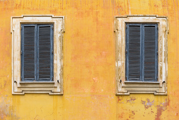 Fototapeta na wymiar Two windows with wooden jalousie on the old stone wall
