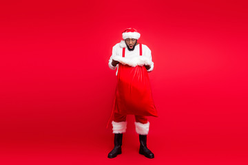 Full length photo of astonished black santa claus looking into his bag screaming omg wow wearing white sweater pants trousers isolated over red background