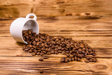 White cup and scattered coffee beans on wooden table