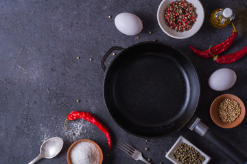 Frying pan and eggs. Empty cast iron pan, eggs, salt, pepper, oil and parsley on black background for cooking fried eggs.