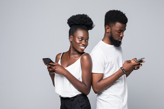 Portrait Of Young Excited African Couple With Mobile Phone Spy Each Other Isolated On Gray Background