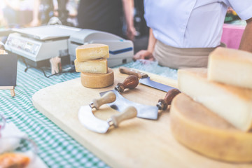 Cheese and cutting equipment on table and salesman in the background on street food market.