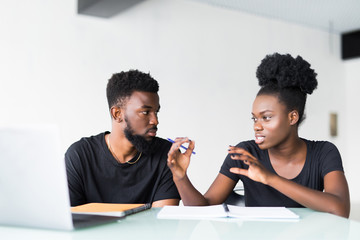 Happy African American couple of enterpreneurs develop new business strategy on portable laptop computer, use mobile phones for surfing information in internet, sit together in office room