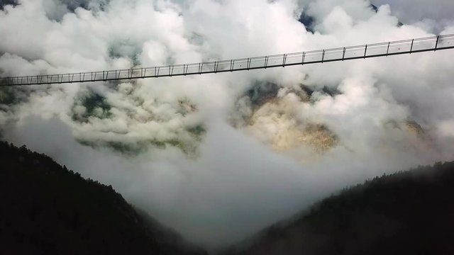 aerial view of people walking on a suspension bridge over a foggy forest.  flying under a suspension bridge. Charles kuonen suspension bridge in randa.