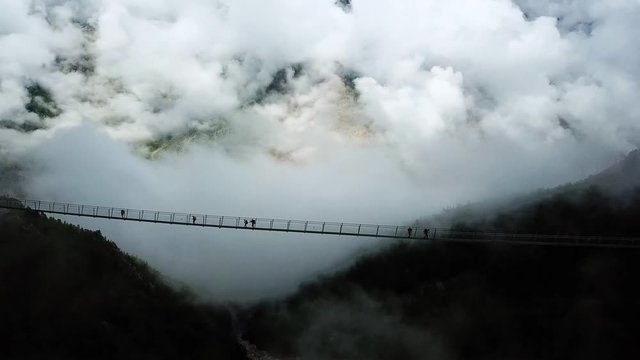 aerial view of people walking on a suspension bridge over a foggy forest. Charles kuonen suspension bridge in randa. longestpedestrian suspension bridge in the world.