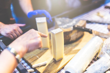 Customer selecting the piece of traditional cheese at market stall.