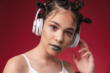 Image closeup of pretty punk girl with bizarre hairstyle and dark lipstick listening to music with headphones