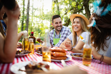 Group of happy friends eating and drinking beers at barbecue dinner