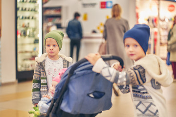 Two brothers with a little sister in a supermarket. they ride a pram while mom is shopping.